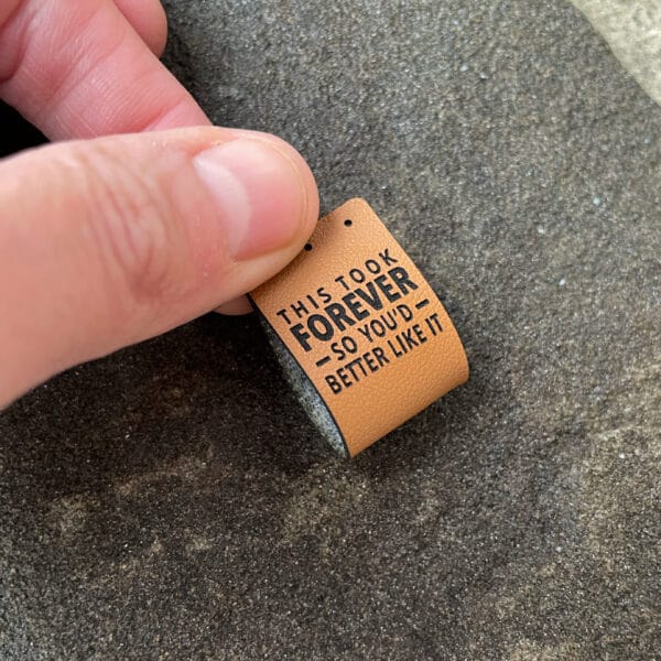 Mixed set of six faux leather tags with 'This took forever so you’d better like it' text. Includes two brim fold, two side-fold, and two flat stitch tags. Available in cinnamon brown or warm gray.